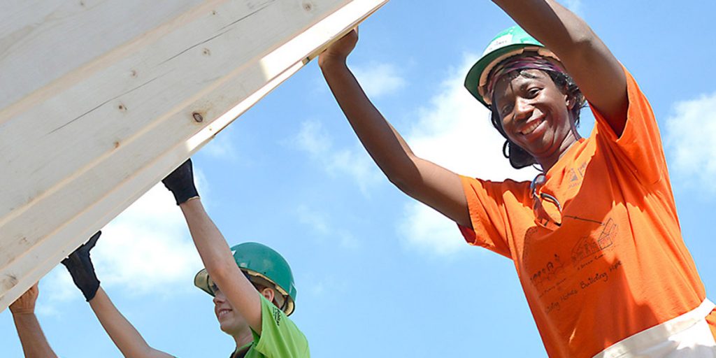 Woman volunteering for Habitat for Humanity smiling while raising a wall for a house